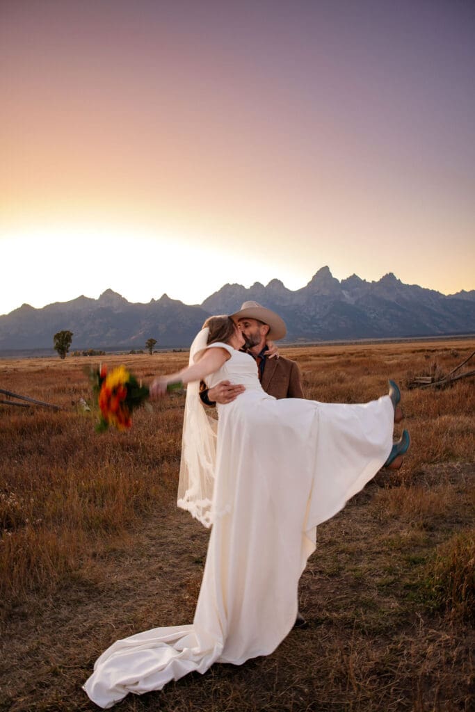 Groom carries bride through mormon row field