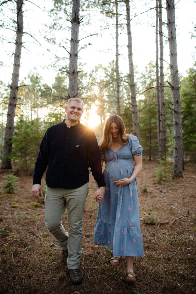 maternity couple walks through the forest at sunset